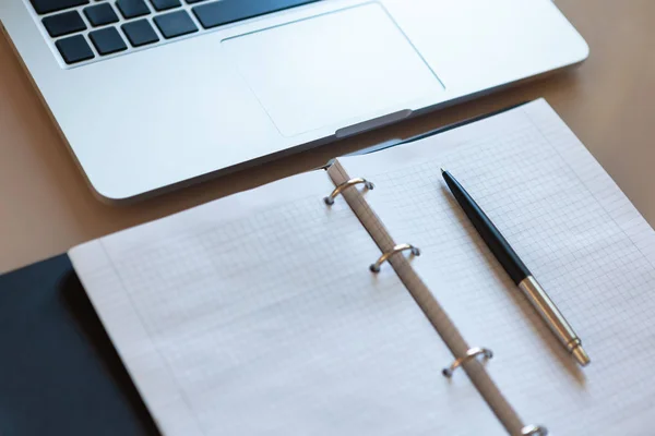 Werkruimte, bovenaanzicht. Laptop en open notebook met pen op beige desktop. Notitieblokjes op zilveren beugels, automatische balpen in zilverkleurige kleur. Bedrijfsachtergrond. — Stockfoto