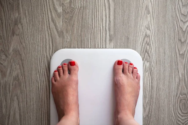 Femme se tient sur blanc moderne balances de capteur électronique. Seuls les pieds sont visibles. Les balances se tiennent sur le plancher en bois gris. Espace pour le texte. Mode de vie sain, régime alimentaire, concept de perte de poids. Horizontal . — Photo