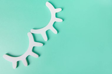 Pastel turkuaz arka plan üzerinde kirpikler ile iki beyaz ahşap kapalı gözleri şeklinde şık duvar dekor. Üst görünüm, düz yatıyordu. Canlı rüyalar kavramı. Çocuk odası için aksesuarlar. Minimal stil