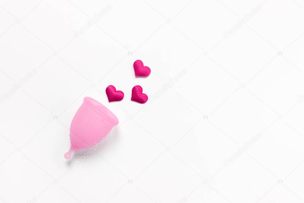 Pink menstrual cup on white background with crimson hearts. Concept zero waste, savings, minimalism, these days. Feminine hygiene product, flat lay, copy space. Horizontal