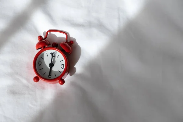 Red analog clock on white rumpled sheets. Top view, flat lay, copy space. Horizontal. Concept of awakening, sleep, early rise, productivity, productive day. For social media, blog. Minimal style.