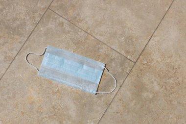 Atılmış mavi tıbbi yüz kalkanı fayans zemininde duruyor. Koronavirüs salgınının, çevresel kirliliğin, zararlı tek kullanımlık çöplerin, insanların bilinçsizliğinin sonuçları. Yatay.