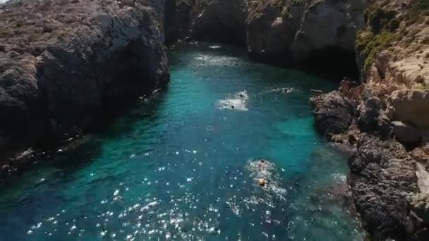 ゴゾ島マルタ 月18日 2018 海の入り江で泳いでいる人々の上のアリエルは 美しい紺碧の色の水と ゴゾ島の Hondoq 湾近くの岩の崖で日光浴をします — ストック動画