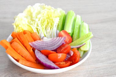 Gri ahşap masada beyaz tabakta taze organik sebzeler. (Kırmızı soğan, domates, salatalık, havuç ve Çin lahanası dilimleri)