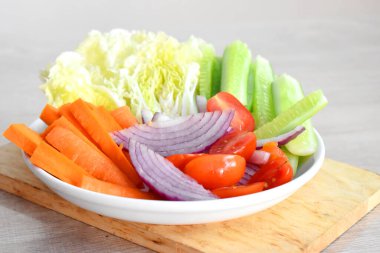 Gri ahşap masada beyaz tabakta taze organik sebzeler. (Kırmızı soğan, domates, salatalık, havuç ve Çin lahanası dilimleri)