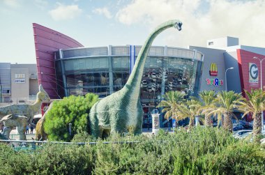 Rishon Lezion, İsrail-Nisan 25, 2017: Gerçek boyutu heykel Park sinema şehir bina önünde küçük bir kafa ile boyun yükselen yeşil Brachiosaurus. Büyük Velafrons başka bir tanınabilir bir hayvandır
