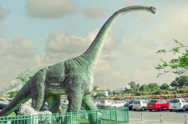 Rishon Letsiyon, İsrail-Nisan 25, 2017: Sinema City ziyaretçi park arabalar için eşsiz bir fırsat yakaladınız yakın Dinosaurs.The dev brachiosaurus 9 metre boyun ile küçük bir kafa çitin üzerinden çıkıntılar ve dikkatli bir şekilde park edilmiş arabalar saatler