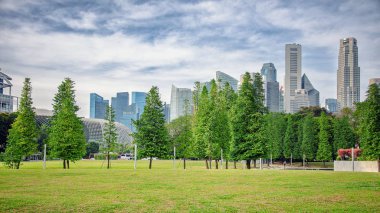 Singapur - 24 Mart 2018: War Memorial Park Beach Road şehir merkezinde çekirdek yer alır. Gnetales gnemon Melinjo ağaçları boyunca yüksek binalar yükselen ile yürüyüş yolları ile açık yeşil çimenler üzerinde arka plan vardır.