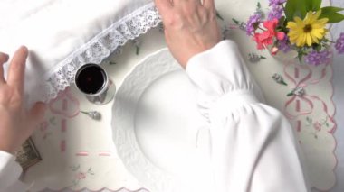 Kadının elleri, Matzo 'yu paketinden çıkartmış ve beyaz bir plakaya yerleştirmeli. Pesach masa bir tatil masa örtüsü ile kaplıdır. Küçük bir vazo içinde bir bardak kırmızı şarap ve çiçekler vardır. Üst görünüm.