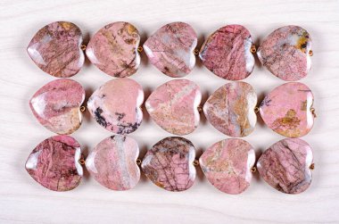 Fifteen rose-pink rhodonite heart-shaped stones are stowed three rows. Five pieces in each one. Top view. clipart