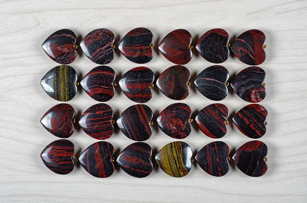 Twenty-four red and iron tiger eye heart-shaped stones are stowed four rows. Six pieces in each one. Top view.