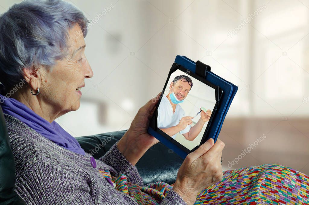 The dental surgeon speaks with an elderly female patient using a telemedicine application. The dentist explains the treatment details on the screen of the senior woman's tablet.