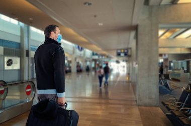 Mavi koruyucu maskeli bir yolcu büyük siyah bir bavulla havaalanına veya tren istasyonuna girdi.