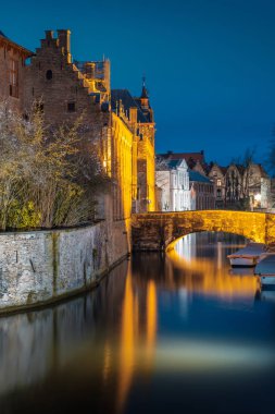 Evening on the streets of Bruges after rain. View of the night Onze Lieve. Brugge against the background of blue evening sky. Belgium. clipart