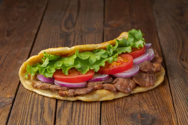 Delicious fresh homemade pita sandwich with roasted meat, tomato, onion and lettuce on dark wooden table.