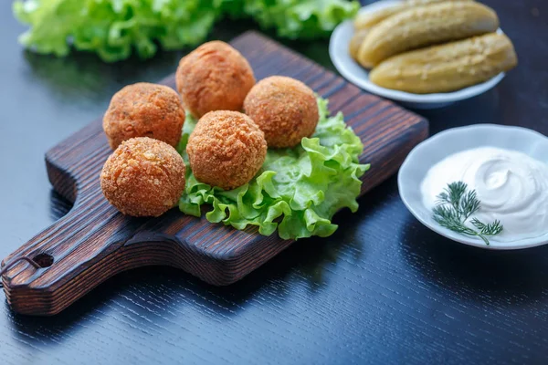 Fried falafel balls on wooden board on table with pickles and sauce