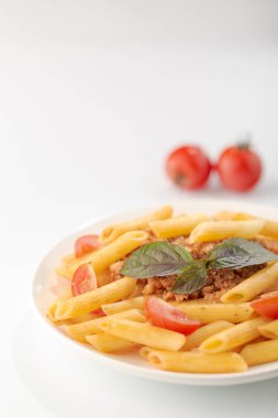 Beyaz arka planda domates ve fesleğen yaprakları ile taze bolonya makarna Tabak
