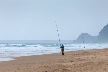 Praia da Mareta, Portekiz fırtınalı havalarda doğal kumlu plajda Adam balıkçılık