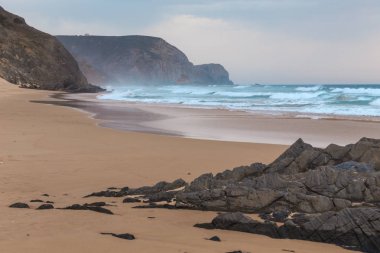 Praia da Mareta fırtınalı havalarda doğal kumlu plajda Rocks, Portekiz