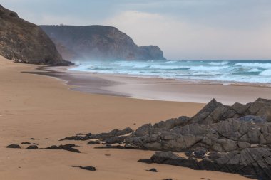 Praia da Mareta fırtınalı havalarda doğal kumlu plajda Rocks, Portekiz