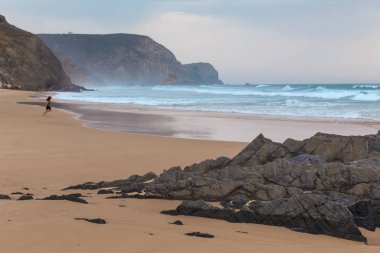 Praia da Mareta fırtınalı havalarda doğal kumlu plajda oynayan çocuk, Portekiz