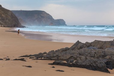 Praia da Mareta fırtınalı havalarda doğal kumlu plajda oynayan çocuk, Portekiz