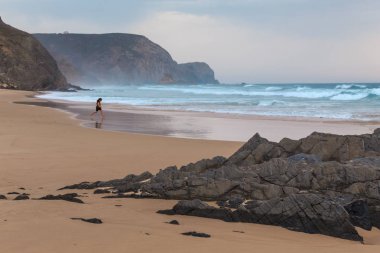 Praia da Mareta fırtınalı havalarda doğal kumlu plajda oynayan çocuk, Portekiz