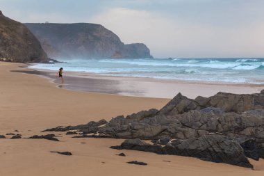 Praia da Mareta fırtınalı havalarda doğal kumlu plajda oynayan çocuk, Portekiz