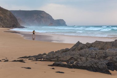 Praia da Mareta fırtınalı havalarda doğal kumlu plajda oynayan çocuk, Portekiz