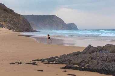 Praia da Mareta fırtınalı havalarda doğal kumlu plajda oynayan çocuk, Portekiz