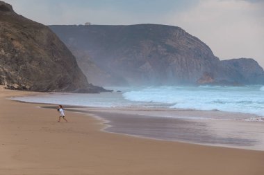 Praia da Mareta fırtınalı havalarda doğal kumlu plajda oynayan çocuk, Portekiz