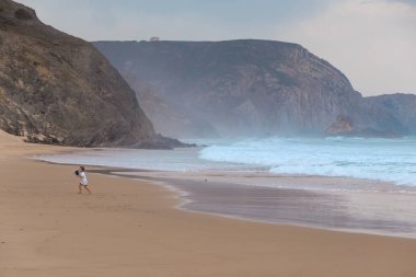Praia da Mareta fırtınalı havalarda doğal kumlu plajda oynayan çocuk, Portekiz