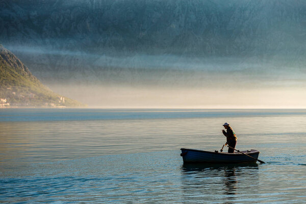 Coastal scenery with fisherman in boat on water in vacation destination of Perast, Bay of Kotor, Montenegro, Europe
