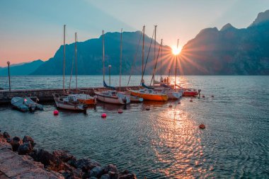Yachts moored at pier during sunset on Lake Garda in mountains, Riva del Garda, Italy, Europe