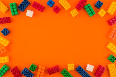 Oyuncak renkli plastik bloklar ve turuncu arka planda renkli oyuncak tuğlalar. Uzayı kopyala Üst görünüm.