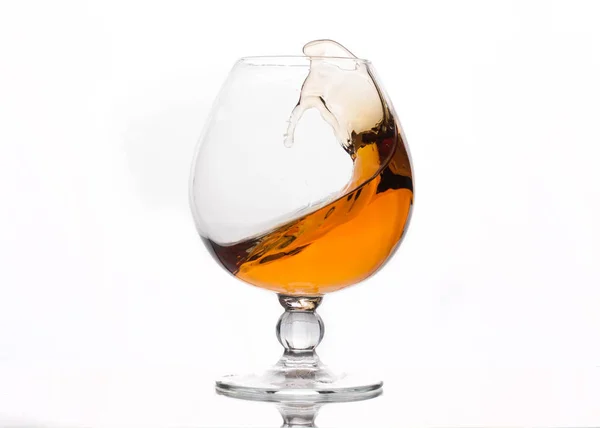 splash of brown cognac in transparent glass with reflection on white