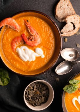 Üstten Görünüm karides, kabak tohumu karanlık kase ve ekmek, siyah arka plan üzerine gümüş kaşık ile turuncu kabak çorbası