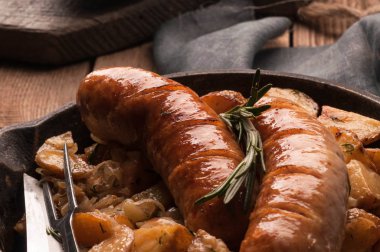 Çatal, bıçak, gri peçete ve ahşap zemin üzerine doğrama tahtası ile kızarmış patates ve tavada ızgara sosis yakın çekim