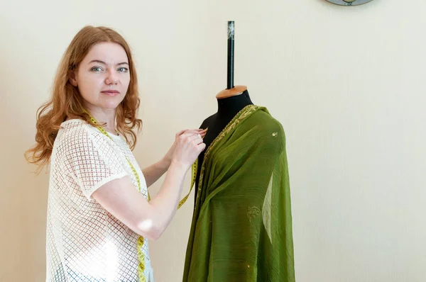 マネキンの近くに立って 布を掛けるとミシン スタジオでカメラを見て魅力的な女性の裁縫師 — ストック写真