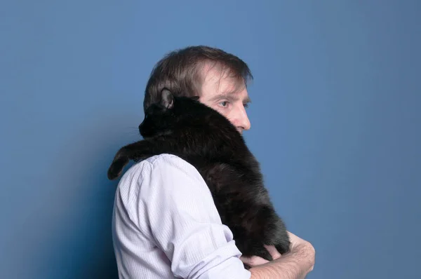 side view of man in shirt and holding and holding black cute cat on sholder on blue background with copy space