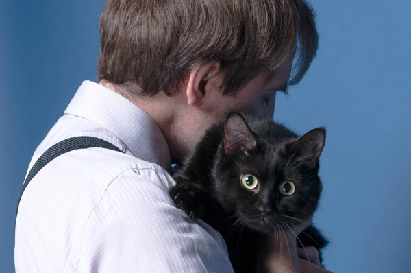 side view of man in pink shirt and suspender holding and hugging black cute cat on blue background with copy space