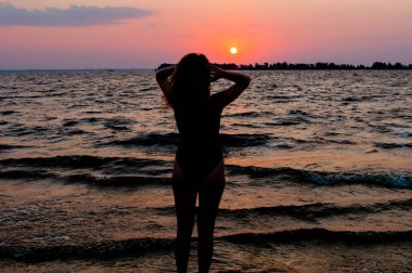 Mayo ayakta ince kadın rakam arka görünümü, saç düzeltme ve sahilde denize yakın inanılmaz gündoğumu bakıyor