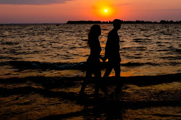 Cherkasy, Ukrayna-08.14.2018: şafakta suda nehir plajında yürüyen kadın ve adamın karanlık siluetleri