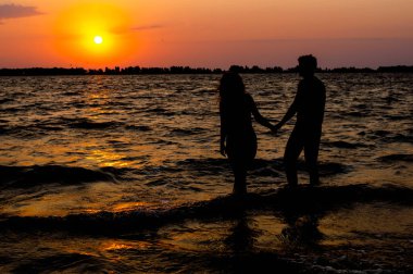 Cherkasy, Ukrayna-08.14.2018: sahilde kadın ve adam silüetlerin arka görünümü güneşin doğuşunda eller tutun
