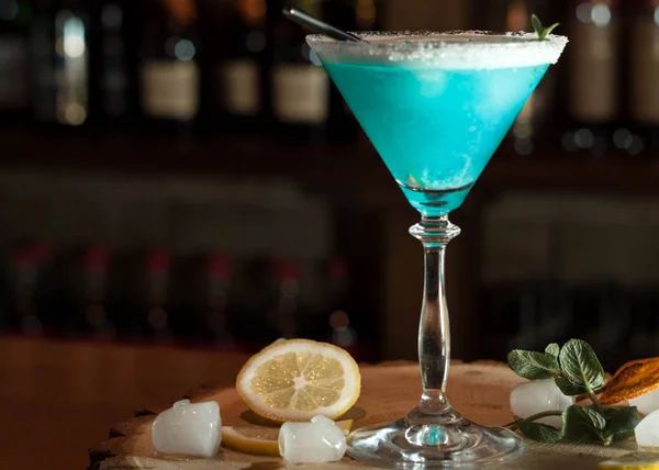 在高茎上的玻璃上的蓝色酒精饮料 在柠檬片 冰和薄荷附近的木制切菜板上用黑色的吸管 — 图库照片