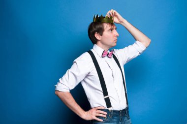 gömlek, askı, kalça el ile Bow kravat yakışıklı adam yan görünümü, uzağa bakıyor ve kopya alanı ile mavi arka planda baş altın taç Düzeltme