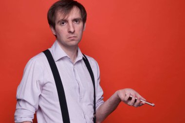 silindir kollu ve siyah askı ayakta, kamera bakarak ve kopya alanı ile turuncu arka planda akıllı telefon tutarak gömleğinde hayal kırıklığına yakışıklı adam