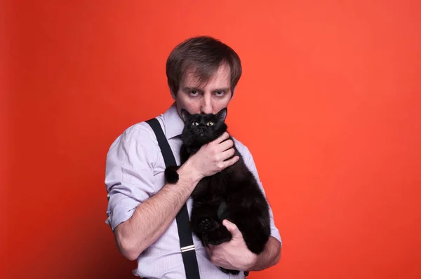 confident man holding and kissing black cat and looking at camera on orange background with copy space