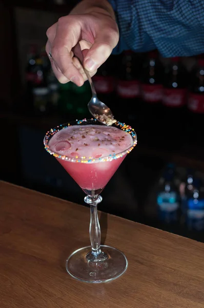 木製のカウンターの近くに立っているバーテンダーのトリミングされたビュー スプーンを保持し バーでガラスで赤いアルコール飲料を飾る — ストック写真