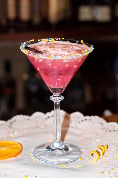 glass with red alcohol drink and straw on white paper napkin with dried orange slice  on table in bar